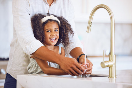 Portrait of a family washing their hands for hygiene, to stop germs and health in the kitchen at home. Happy, smile and father helping his child clean her hand of bacteria, dirt and dust in a house.の写真素材