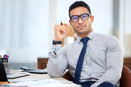 Young mixed race businessman going through a report alone in an office at work. One focused hispanic male businessperson sitting at a desk in an officeの写真素材