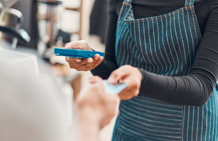 Closeup of a clerk accepting a credit card payment from a customer in a cafe or store. Hands of woman using card machine reader while taking money for a purchase transaction from a man in a shopの写真素材