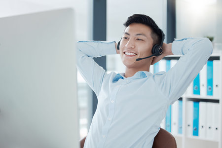 Call center, computer or relax man in success sales deal, customer support crm or consulting help in Vietnamese b2b office. Happy smile, telemarketing or contact us technology receptionist stretchingの写真素材