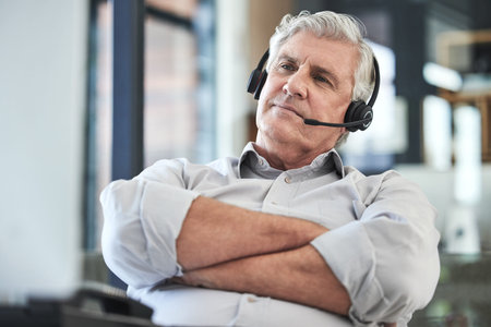 This requires some thought. a mature call centre agent sitting alone in the office with his arms...