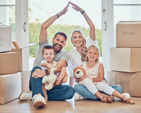 Smiling couple with little kids sitting and making symbolic roof with hands over children. Cheerful family sitting together on floor in new house on relocation day. Covered and protected by insuranceの写真素材