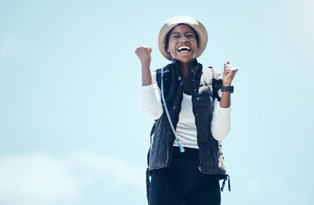Winner, happy and black woman celebrate fitness journey out in nature on hike, victory during adventure. Success, blue sky and travel, laugh and freedom, carefree health and active lifestyle.の写真素材