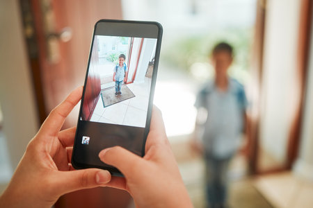 Closeup of mother taking photo of son on first day of school. Hands taking picture on cellphone of kindergarten boy standing by the door and ready to leave home. Proud mom documenting childhoodの写真素材
