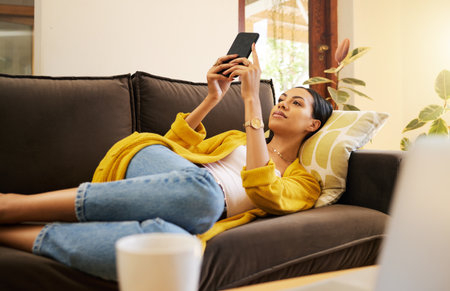 Relax woman on her phone with social media while on the sofa in house. Content female browsing internet with app while relaxing on the couch at home reading news, post and internet or webの写真素材