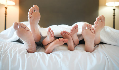 Cozy family lying in bed relaxing sleeping together. Feet and toes of parents and their tired little children sleeping taking a nap under a blanket in bed at homeの写真素材