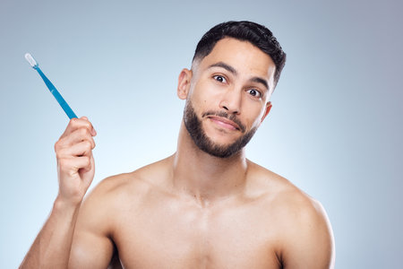 One brush away from perfection. a young man holding a toothbrush against a studio background.の写真素材