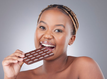 Heavens made of chocolate. Studio shot of an attractive young woman eating a slab of chocolate against a grey background.の写真素材