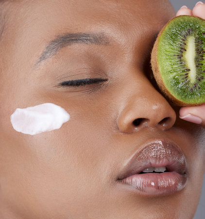 Perfect day for a pamper session. Studio shot of an attractive young woman holding kiwi fruit to her...