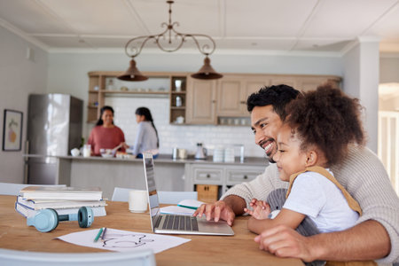 Happy young mixed race father and daughter using a laptop while sitting at a table together in the lounge at home. Hispanic dad and child looking at a laptop screen. Little girl bonding with her dadの写真素材