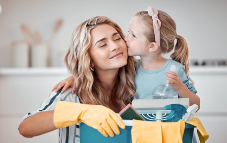 Little caucasian girl kissing mom on cheek while helping with household chores at home. Happy mother and daughter excited to do spring cleaning together. Kid learning to be responsible by doing tasksの写真素材