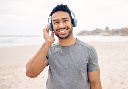 I feel less stressed when Im outdoors. Portrait of a sporty young man wearing headphones while exercising on the beach.の写真素材