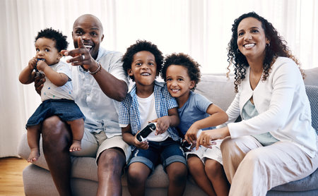 Sibling brothers playing video games together while sitting with their family. African american...