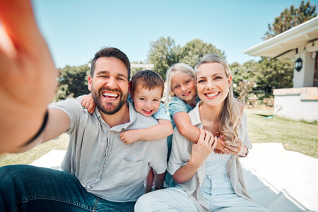 Portrait of happy family with little kids taking selfies in a garden. Smiling caucasian couple bonding with their son and daughter in a backyard. Adorable girl and boy enjoying free time with parentsの写真素材