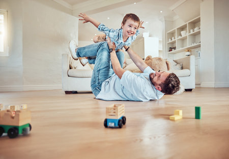 Father lifting his son. Dad lying on the floor lifting his child. Little boy flying in dads arms. Excited father playing with his kid. Father and son bonding in the lounge at home.の写真素材