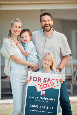 Portrait of happy caucasian family holding for sale and sold sign while relocating and moving in new house. Smiling parents and kids securing homeowner loan for property real estate and home purchaseの写真素材