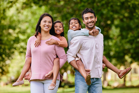 Portrait of happy asian family standing close together in a park. Adorable little girls enjoying free time with their mother and father on a weekend outside. Smiling mixed race couple embracing theirの写真素材