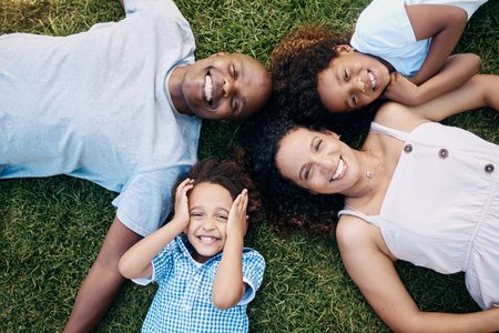 Above view of cheerful african american family lying in a circle. Dad, mom and their two lovely children lying on the grass looking at camera. Little boy and girl having fun with parents at parkの写真素材
