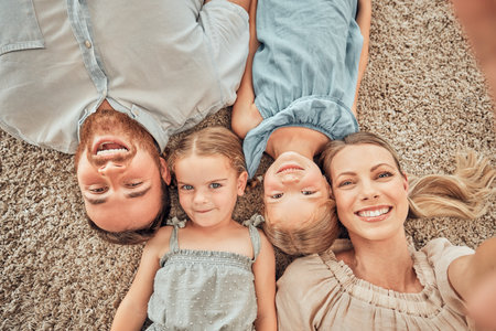 Above shot of a happy and loving family of four taking selfies while lying on their living room floor at home. A beautiful wife taking pictures with her husband, son and daughter while on a carpetの写真素材