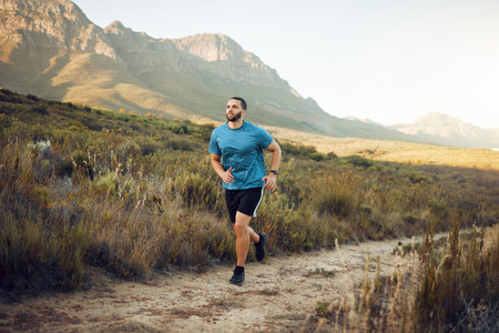 Health, mountain and man running in nature for fitness, training and sports exercise. Workout, wellness and summer with athlete runner in grass field path for peace, marathon and outdoor morning jogの写真素材