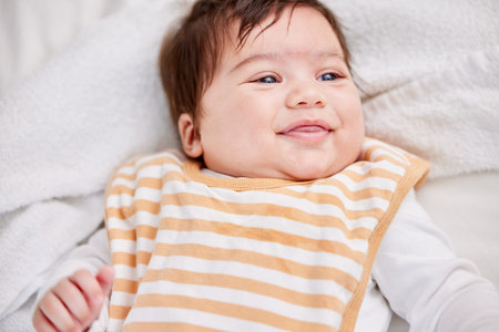 Cute little baby playful and smiling while lying on the bed in a bedroom. Small hispanic baby...