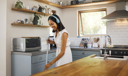 Happy, headphones and woman cleaning the kitchen while listening to music, podcast or radio. Happiness, smile and girl cleaner or housewife washing the floors in a modern home, house or apartment.の写真素材
