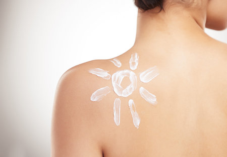 Back of a beautiful woman showing her applying cream on her shoulder posing against a grey copyspace...