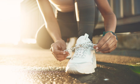 Closeup of one mixed race woman tying her shoelaces while exercising outdoors. Athlete fastening...