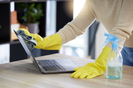 Laptop, cleaning and hands with an office cleaner wiping a computer on a desk or table with sanitizer. Hygiene, disinfectant and rubber gloves with a woman dusting or washing wireless technologyの写真素材
