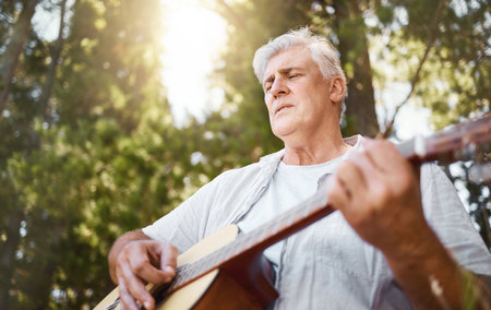 Nature inspires. a handsome mature man playing the guitar while camping in the woods.の写真素材