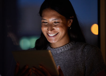 Alls looking well this evening. a young businesswoman using a digital tablet in an office at night.の写真素材