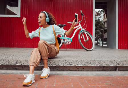 Black woman in city, listen to music on headphones and relax on street sidewalk waiting for a taxi. Girl streaming podcast, musician online and happy dance song from smartphone 5g internet connectionの写真素材