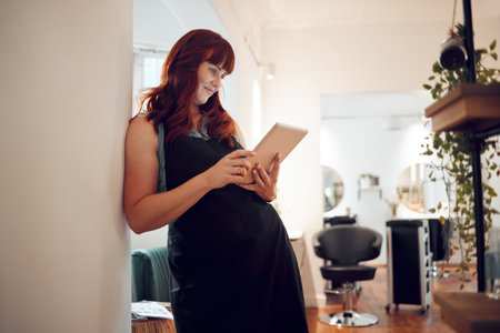 Salon, tablet and schedule with a woman hairdresser checking her appointment or online booking. Calendar, technology and stylist with a female worker or small business owner in the hair care industryの写真素材