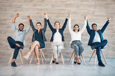 We win together, we lose together. Full length shot of a diverse group of businesspeople sitting together and holding hands while raising them.の写真素材