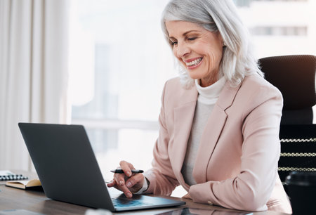 Always an email away. a mature businesswoman sitting alone in the office and using her laptop.の写真素材