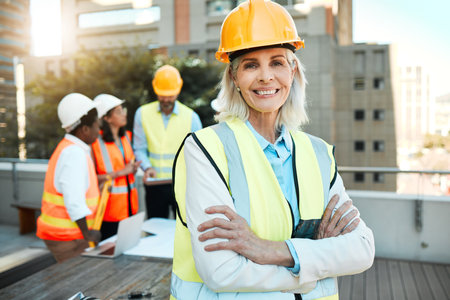 My team are the best. a mature contractor standing outside with her arms folded while her colleagues work behind her.の写真素材