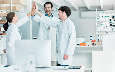 Thrilled by their teams discovery. a group of young scientists giving each other a high five in a lab.の写真素材