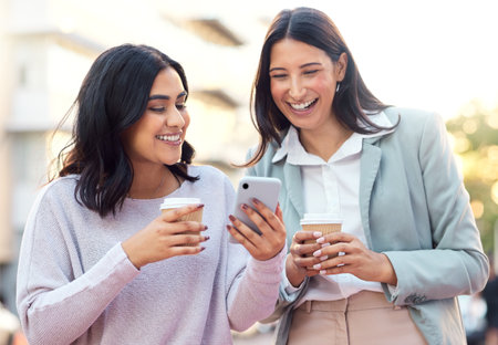 Capitalise on your network and wealth will come. two young businesswomen using a smartphone against an urban background.の写真素材