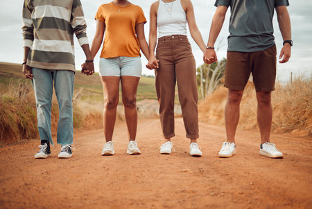 Legs, diversity and people holding hands together in solidarity, connection or support. Trust, friendship help and outdoor desert group, team or friends walk, travel or stand in countryside dirt roadの写真素材