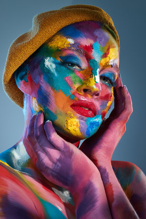 Make the colours dance. Studio shot of a young woman posing with multi-coloured paint on her face and a french hat on her head.の写真素材