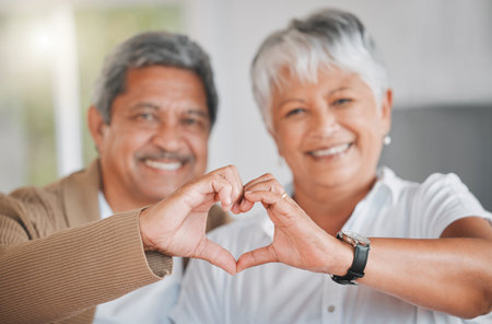 Our hearts are all for each other. Portrait of a senior couple making a heart shape with their hands at home.の写真素材