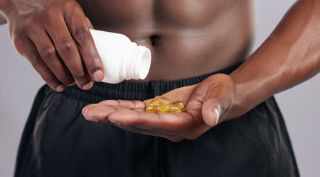 Take your vitamins daily. an unrecognsiable man standing alone in the studio and taking supplements.の写真素材