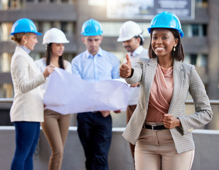 Architects who care. a young female architect showing a thumbs up while working with coworkers against a city background.の写真素材