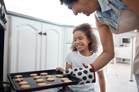 Golden brown just the way I like them. a mature woman inserting a tray of cookies she baked with her granddaughter into an oven.の写真素材