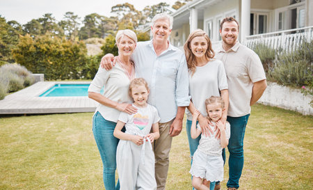Portrait of multi-generation family standing together outside by the pool at home on a sunny day and...