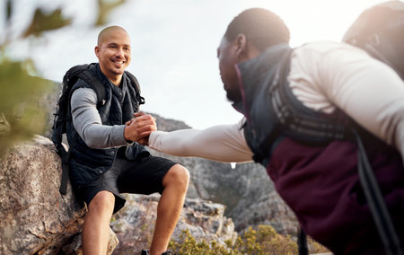 Helping out a friend. a handsome young man helping his friend along a mountain during their hike.の写真素材