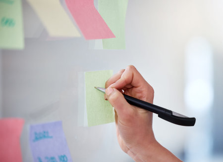Closeup of unknown business woman writing on sticky notes on a transparent board to brainstorm in an...