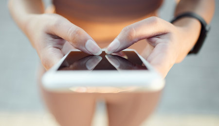 Lets see how many miles Ive ran. Closeup angle shot of an unrecognisable woman using a cellphone while exercising outdoors.の写真素材