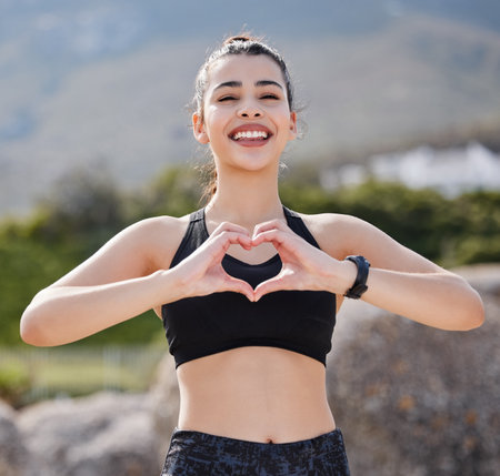 Good times, healthy vibes. Portrait of a fit young woman making a heart shaped gesture after going for a run outdoors.の写真素材