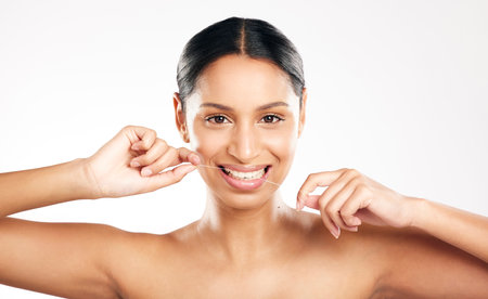 Im flossy. Studio portrait of an attractive young woman using dental floss against a grey background.の写真素材